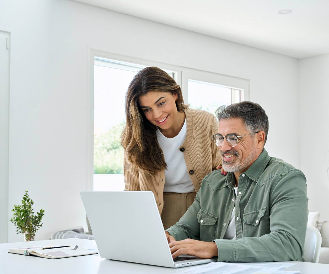 Smiling couple sitting at a desk using a laptop to research buying a home in the United States as non-U.S. citizens