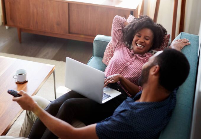 Couple relaxing on couch with laptop researches down payment assistance.