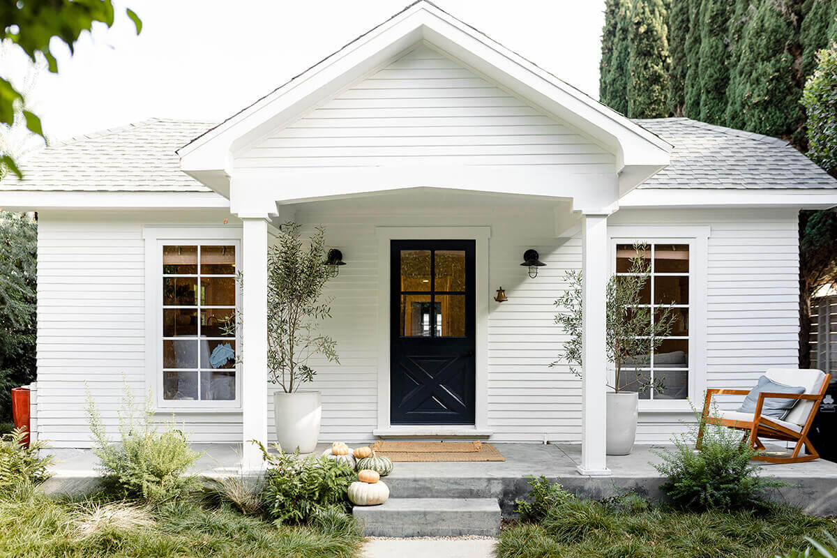 A white cottage with black front door and fall decor, a home secured with earnest money during the homebuying process.