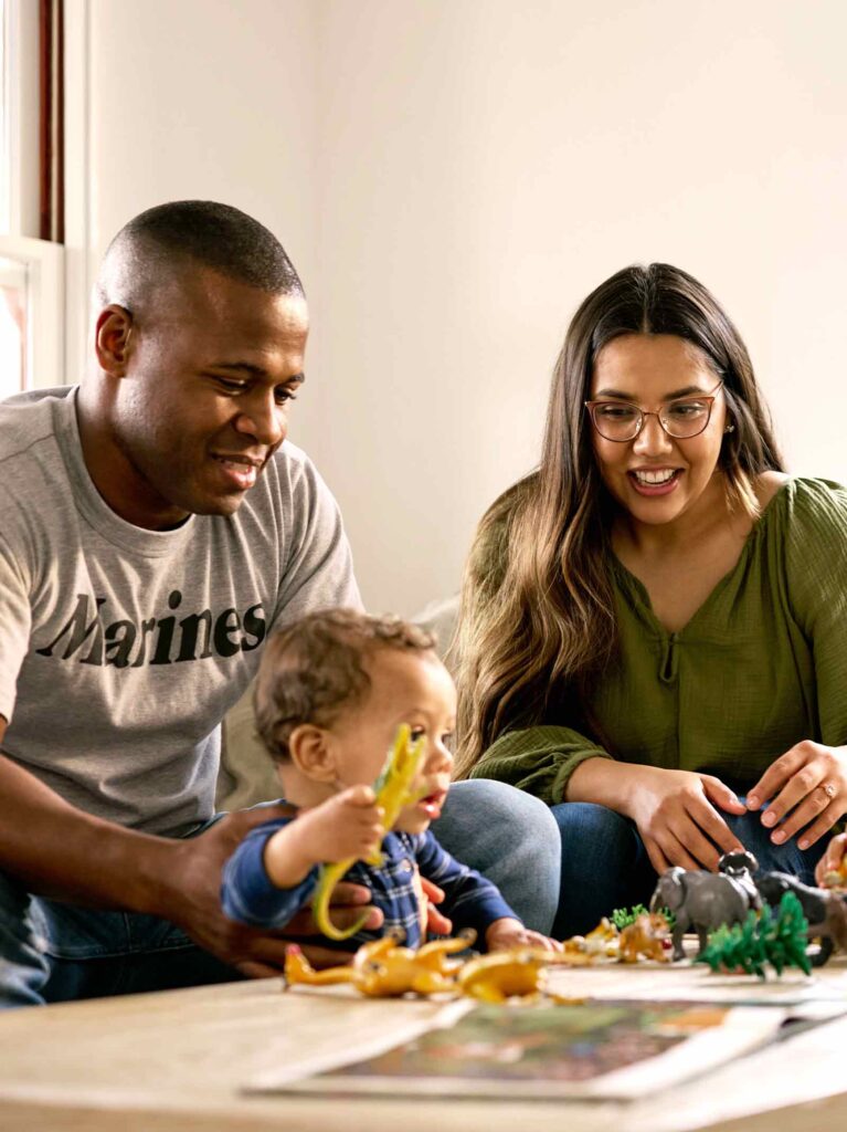 Family of five sits around living room table while playing with dinosaurs.