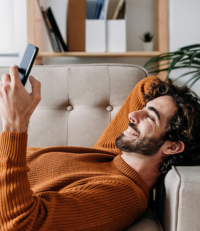 Man relaxing on couch in living space reads about Bye-Bye PMI product on cell phone.