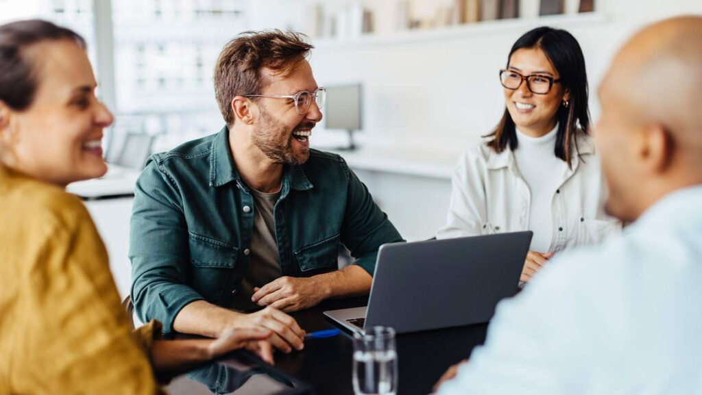 Branch manager and loan officers sit around office table together during meeting at mortgage lending office.