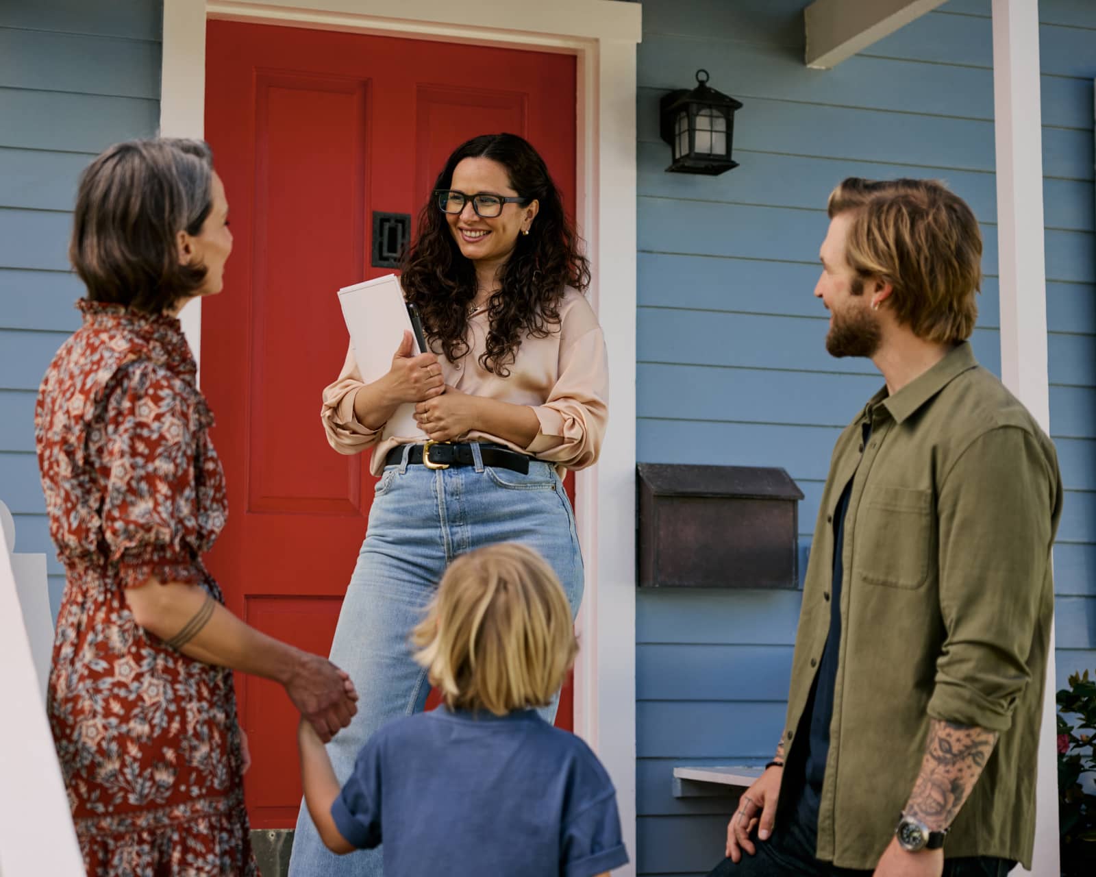 Realtor meets with a first-time homebuyer family outside of blue home for sale.