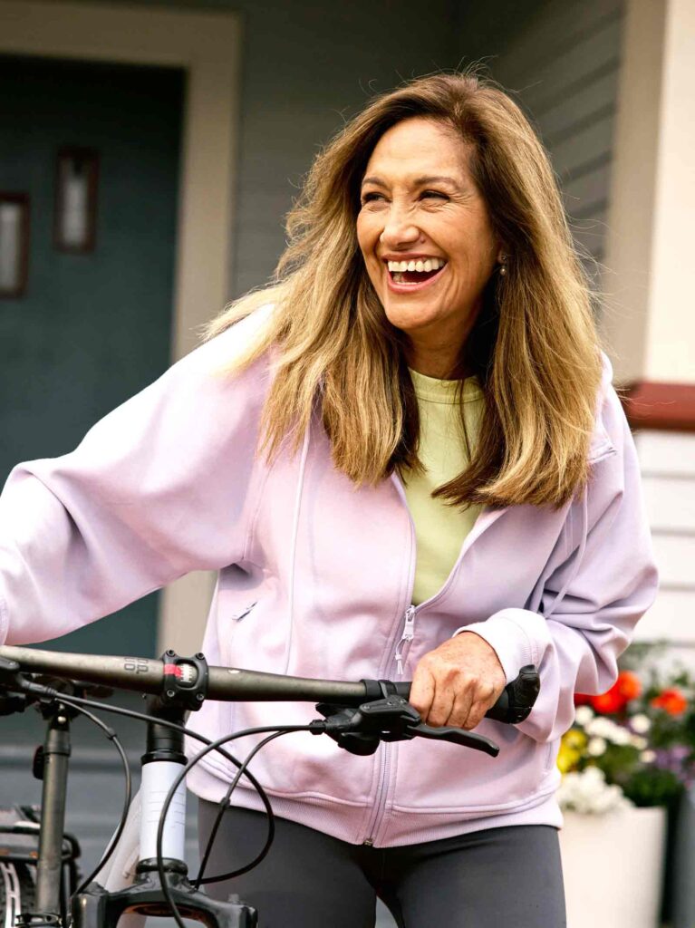 Retired woman on bicycle smiles in front of home financed using reverse mortgage.