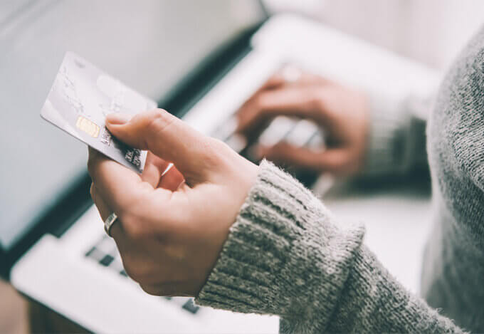 Close-up of a person in a gray sweater holding a credit card and typing credit score details on a laptop.