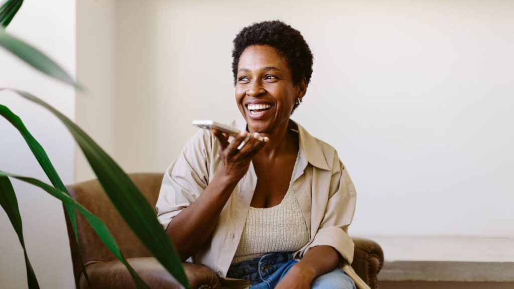 Woman on cell phone sitting on couch asks loan officer if she can buy a house.