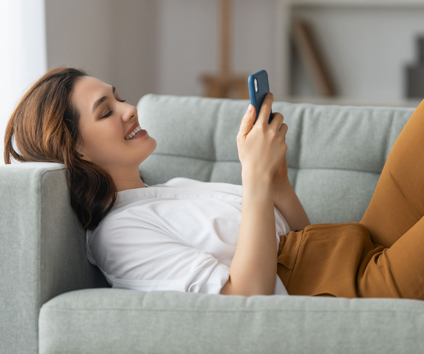 Woman laying on couch enters a mortgage pre-approval into her cell phone.