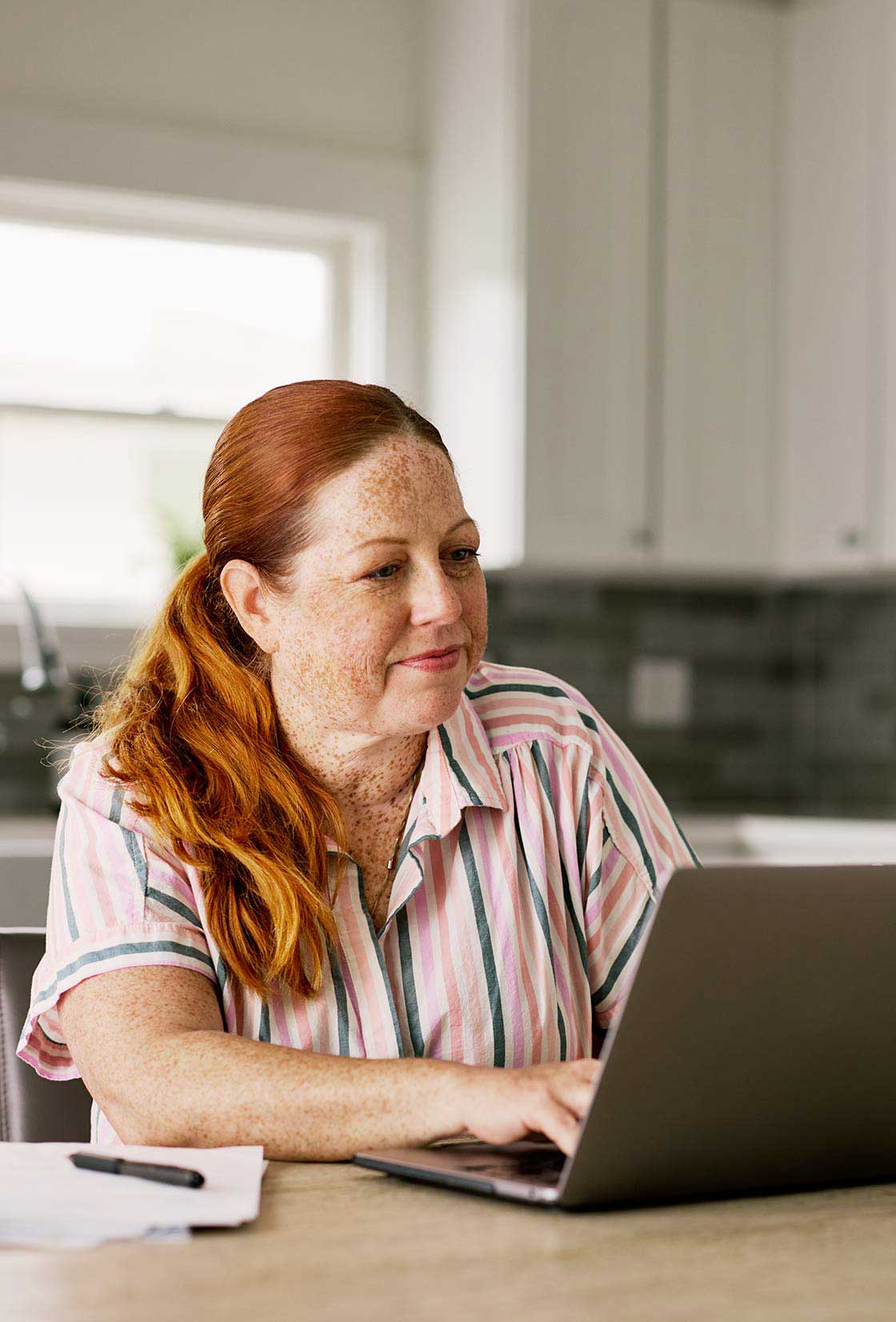 Women sits at kitchen table and researching options to help her purchase a home instead of renting one.